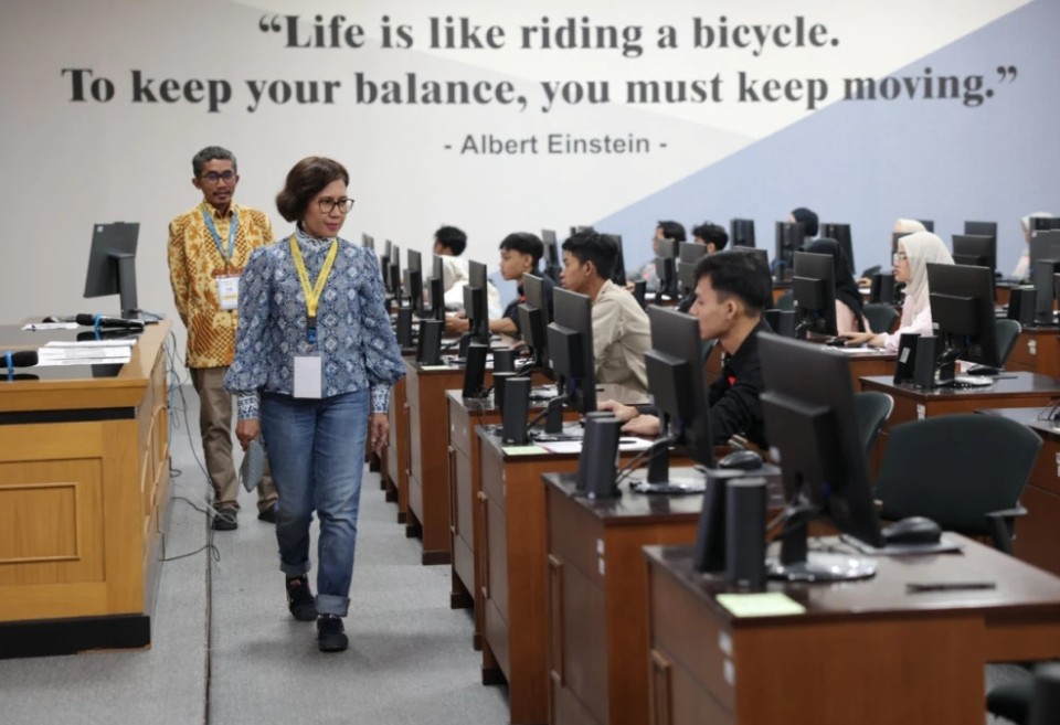 Two instructors walk through a computer lab as students work at desks with an einstein quote on the wall life is like riding a bicycle